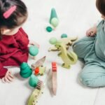 Two children engaged in imaginative play with wooden dinosaur toys on the playroom floor.