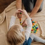 Inicio Top view of a child and adult playing with colorful toy blocks on a beige mat indoors.